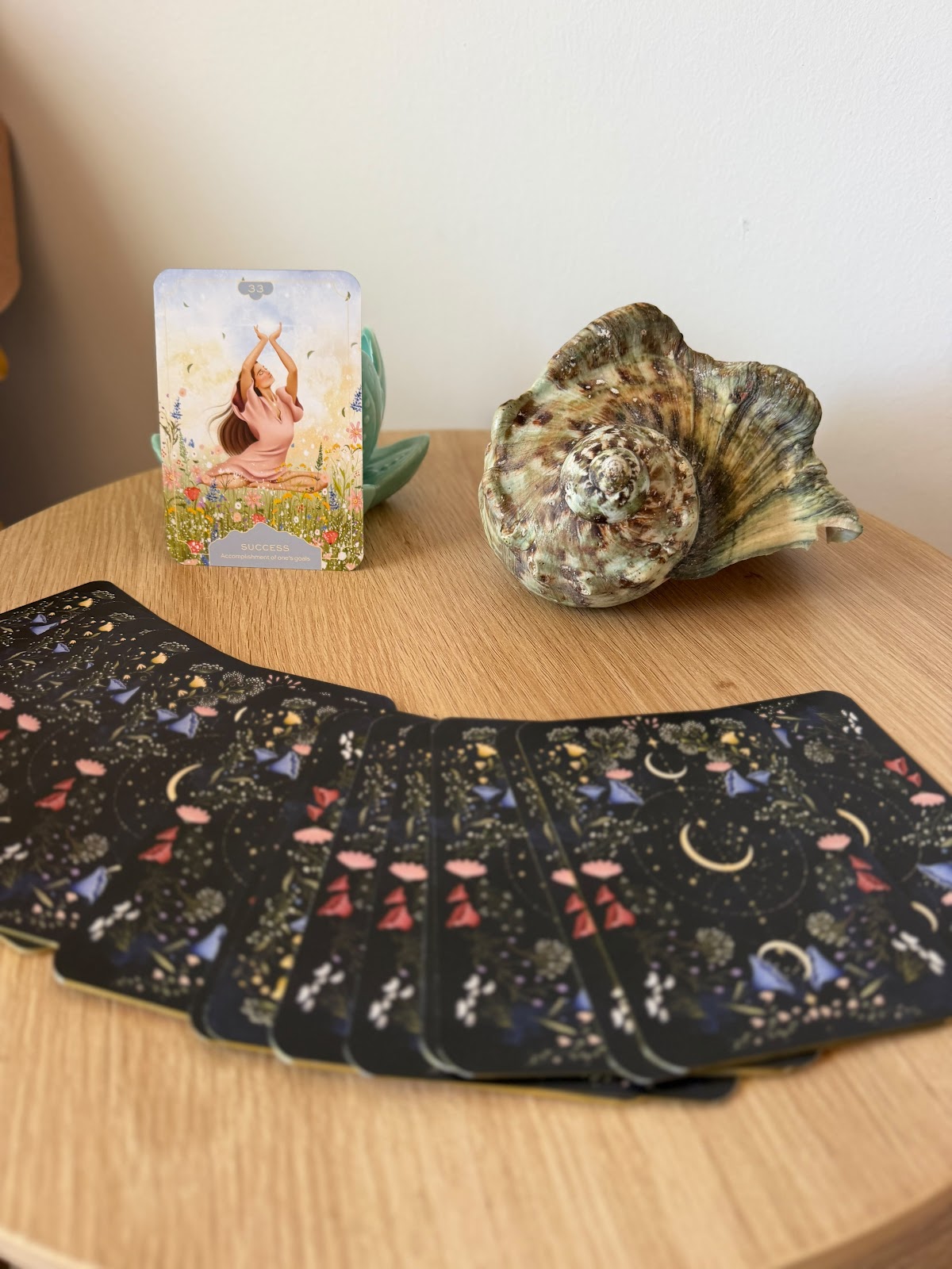 Oracle cards fanned out on a round timber table beside an abalone shell